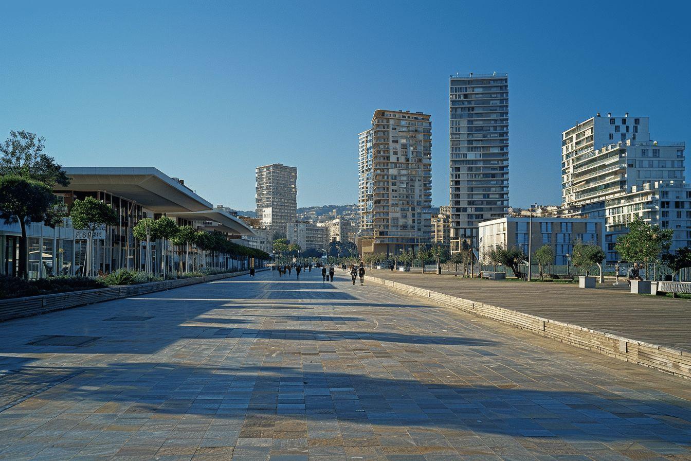 Ville moderne avec gratte-ciel, allée piétonne bordée d'arbres et de bâtiments.